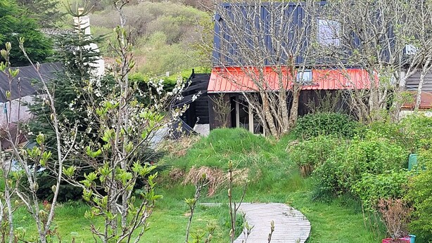 A rural house with a red roof, surrounded by lush greenery and a winding path. - The Quarterdeck (Portree)