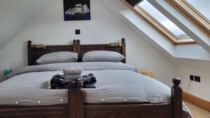 A bedroom with a sloped ceiling and skylight, a wooden bed with striped bedding, and a small bedside table. - The Quarterdeck (Portree)