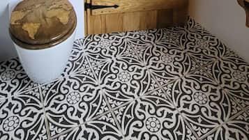 A bathroom with a wooden door, a toilet with a decorative lid, and patterned floor tiles.