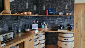 A kitchen with wooden cabinets, a microwave, and a kettle. There are shelves with various kitchen items and a blackboard wall with sailboat drawings. - The Quarterdeck (Portree)