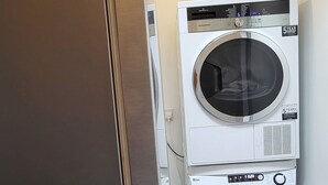 A laundry room with two stacked front-loading washing machines and a modern light fixture. - The Quarterdeck (Portree)