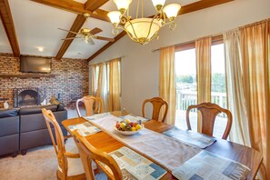Zona pranzo con tavolo in legno, sedie, un lampadario e un camino in mattoni.