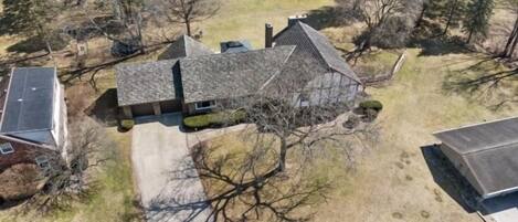 An aerial view of a residential property with a detached house, a driveway, and surrounding trees.