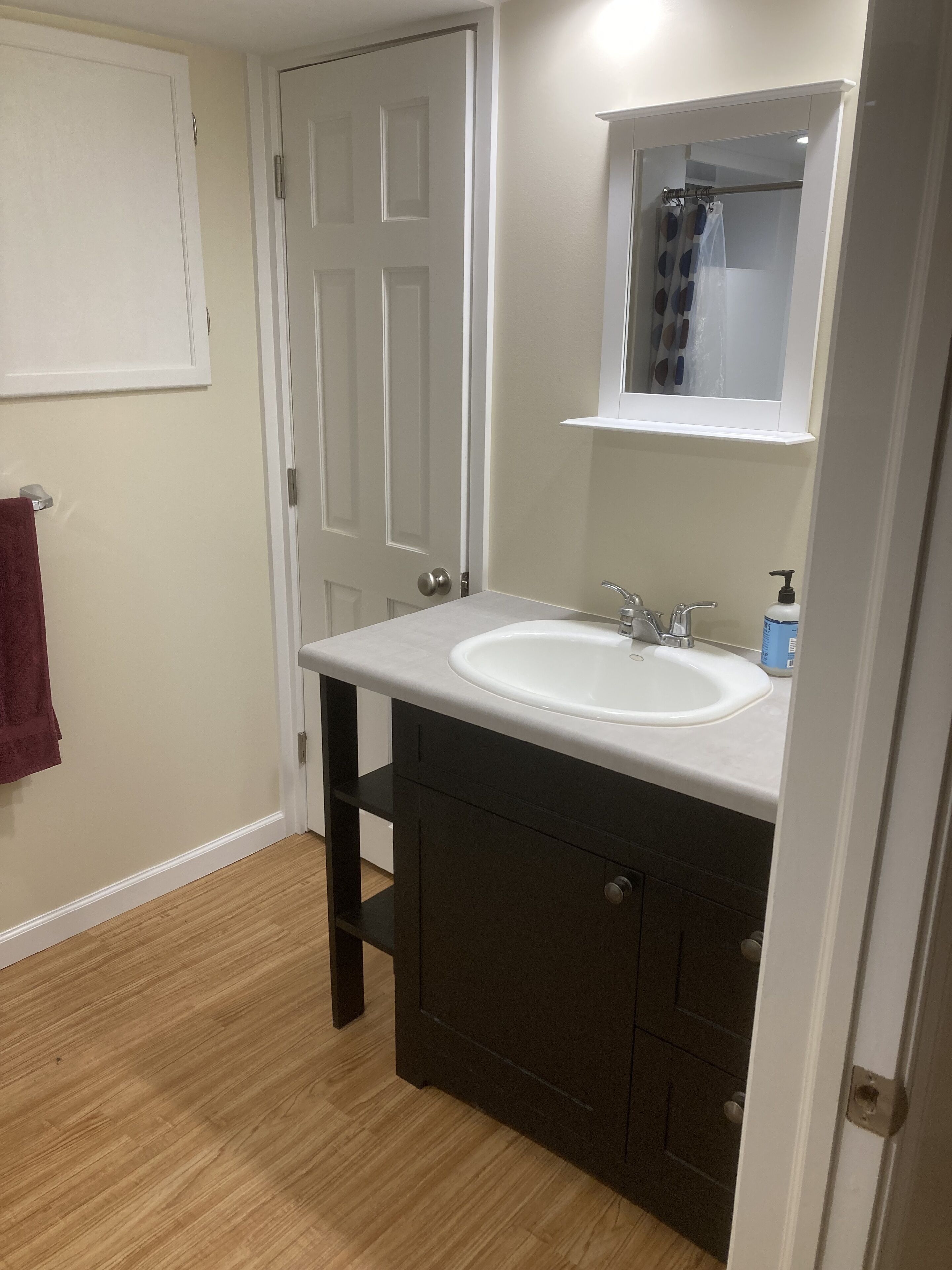 Une salle de bain avec un lavabo blanc, des meubles sombres et un plancher en bois.