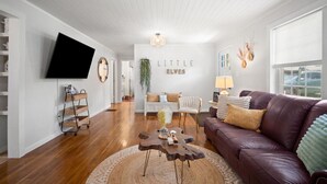 Una sala moderna con un sofá de cuero, una mesa de centro, un televisor y un letrero que dice "LITTLE ELVES".