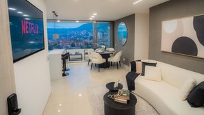 A modern living room with a sofa, coffee table, and dining area. A large TV screen displays the Netflix logo. The room has a city view through large windows. - Apartment Luxe with view of Poblado (Envigado)