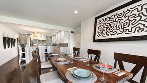 A dining area with a long wooden table set for four, surrounded by chairs.