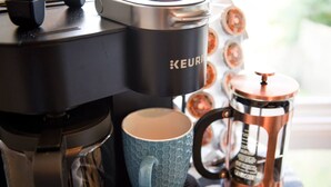 A Keurig coffee maker, a blue mug, and a copper coffee pot on a table.