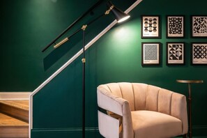 Una escalera de diseño moderno, un sillón color beige y una pared con patrones geométricos enmarcados.