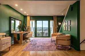 A modern living room with a large window, a desk, a sofa, and a patterned rug.