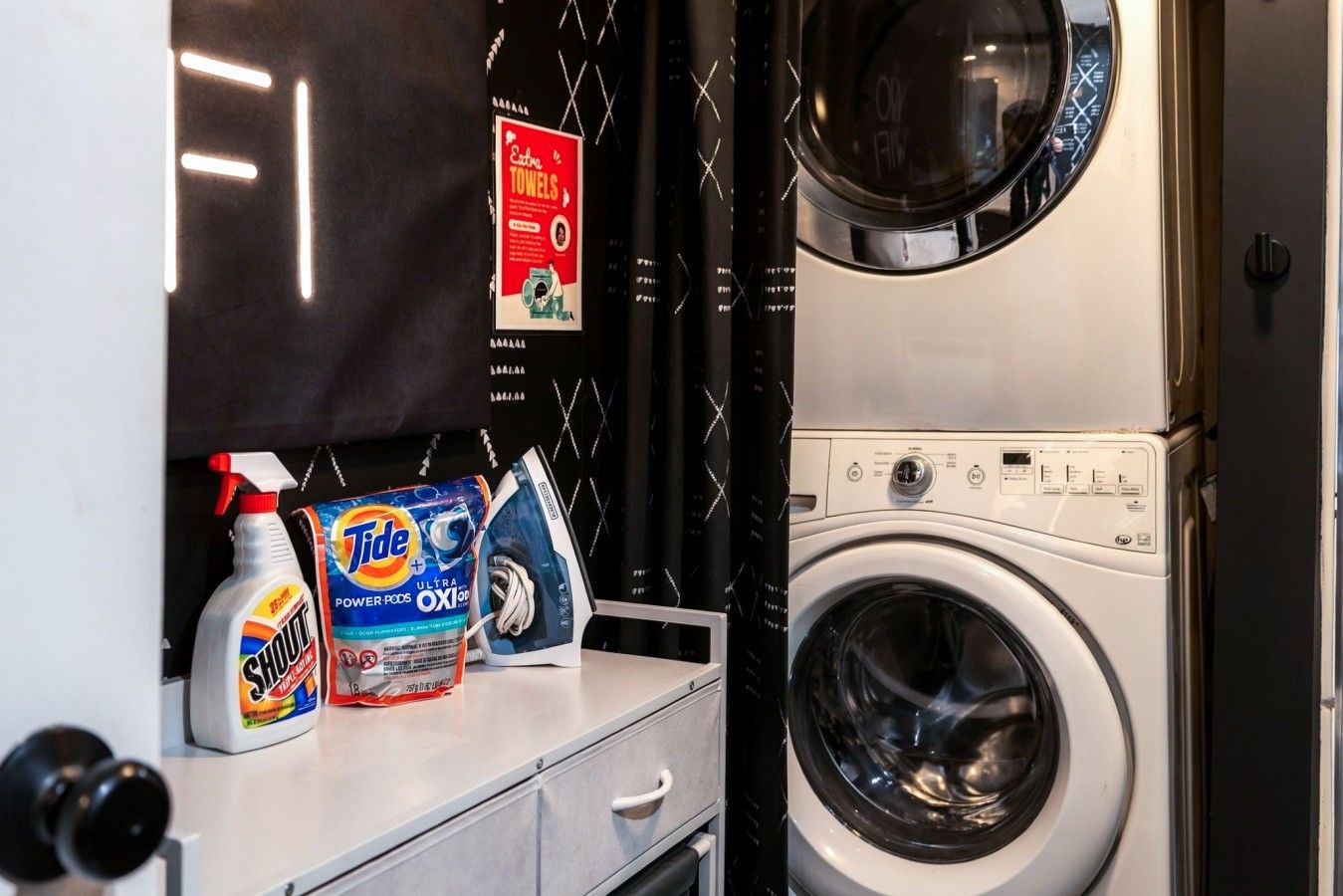 A laundry area with a washing machine, Tide detergent, and a spray bottle.