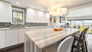 A modern kitchen with a marble countertop, white cabinets, and a large window offering a city view. - City View Sanctuary ~ Hot Tub, Abundant Parking, 3 Decks, Fenced Yard, Fire Pit (Pittsburgh)
