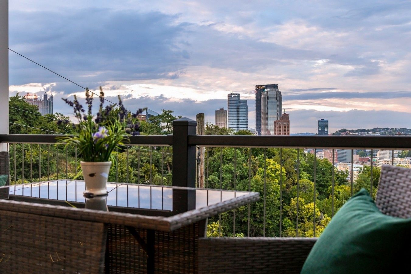 A balcony with a view of a city skyline, a potted plant, and a wicker table.