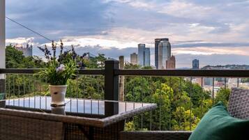 A balcony with a view of a city skyline, a potted plant, and a wicker table.
