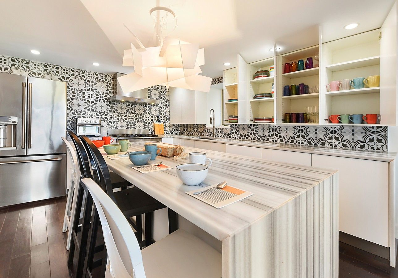 A modern kitchen with a central island, white cabinetry, and a patterned backsplash.