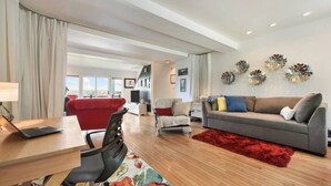 A modern living room with a red sofa, grey sofa, and a red rug. There is a laptop on a wooden table, and a TV on a stand. - City View Sanctuary ~ Hot Tub, Abundant Parking, 3 Decks, Fenced Yard, Fire Pit (Pittsburgh)