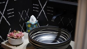 A black metal bowl with white lines, a white pot with pink flowers, and a tissue box on a shelf.