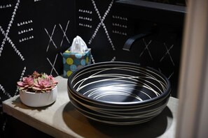 A black metal bowl with white lines, a white pot with pink flowers, and a tissue box on a shelf. - City View Sanctuary ~ Hot Tub, Abundant Parking, 3 Decks, Fenced Yard, Fire Pit (Pittsburgh)