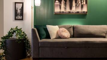 A room with a green wall, a grey sofa with cushions, a floor lamp, and a framed picture of a cityscape.