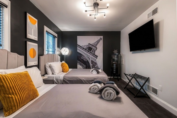 Un dormitorio moderno con dos camas, un ventanal grande, obras de arte en las paredes y un televisor de pantalla plana.