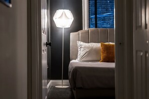 Un dormitorio con una cama, una lámpara de noche y una ventana con persianas.