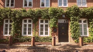 Un bâtiment en briques doté de nombreuses fenêtres et d’une porte noire, le tout entouré de lierre.