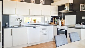 Moderni keittiö, jossa on valkoiset kaapit, sisäänrakennettu uuni ja ikkuna tiskialtaan yläpuolella.