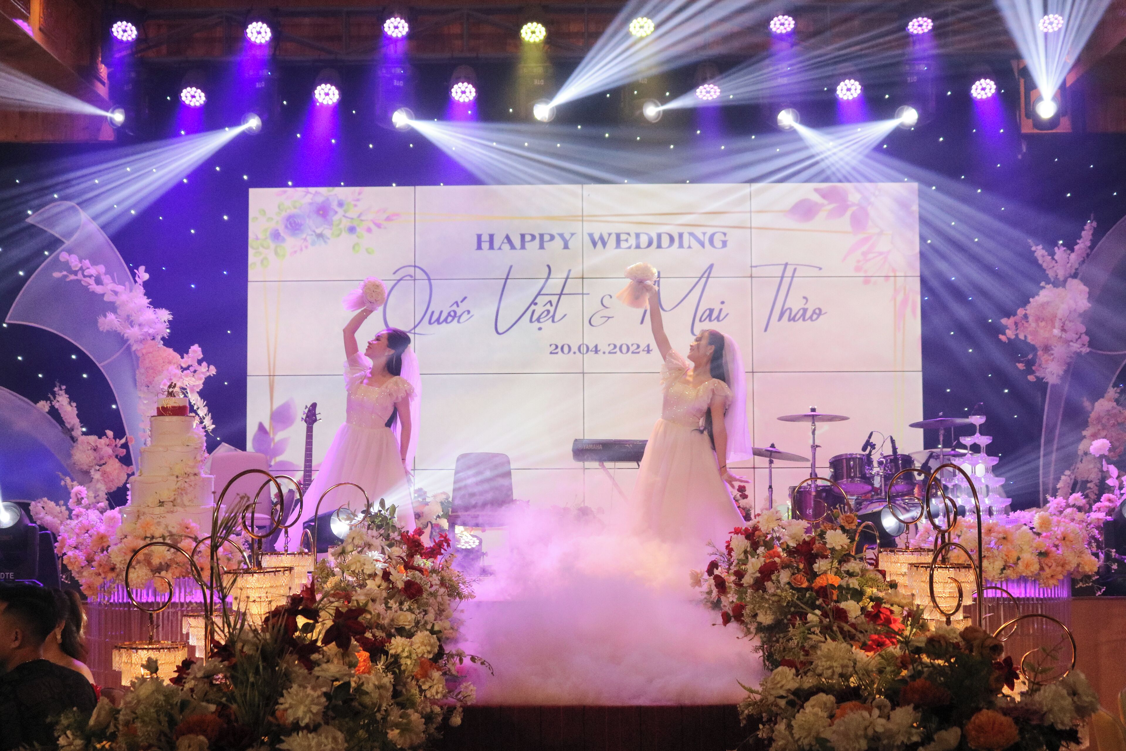 A wedding stage with a backdrop that reads "HAPPY WEDDING Quoc Viet & Mai Thao 20.04.2024".