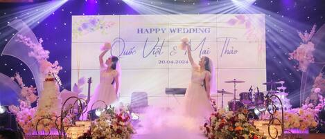 A wedding stage with a backdrop that reads "HAPPY WEDDING Quoc Viet & Mai Thao 20.04.2024".