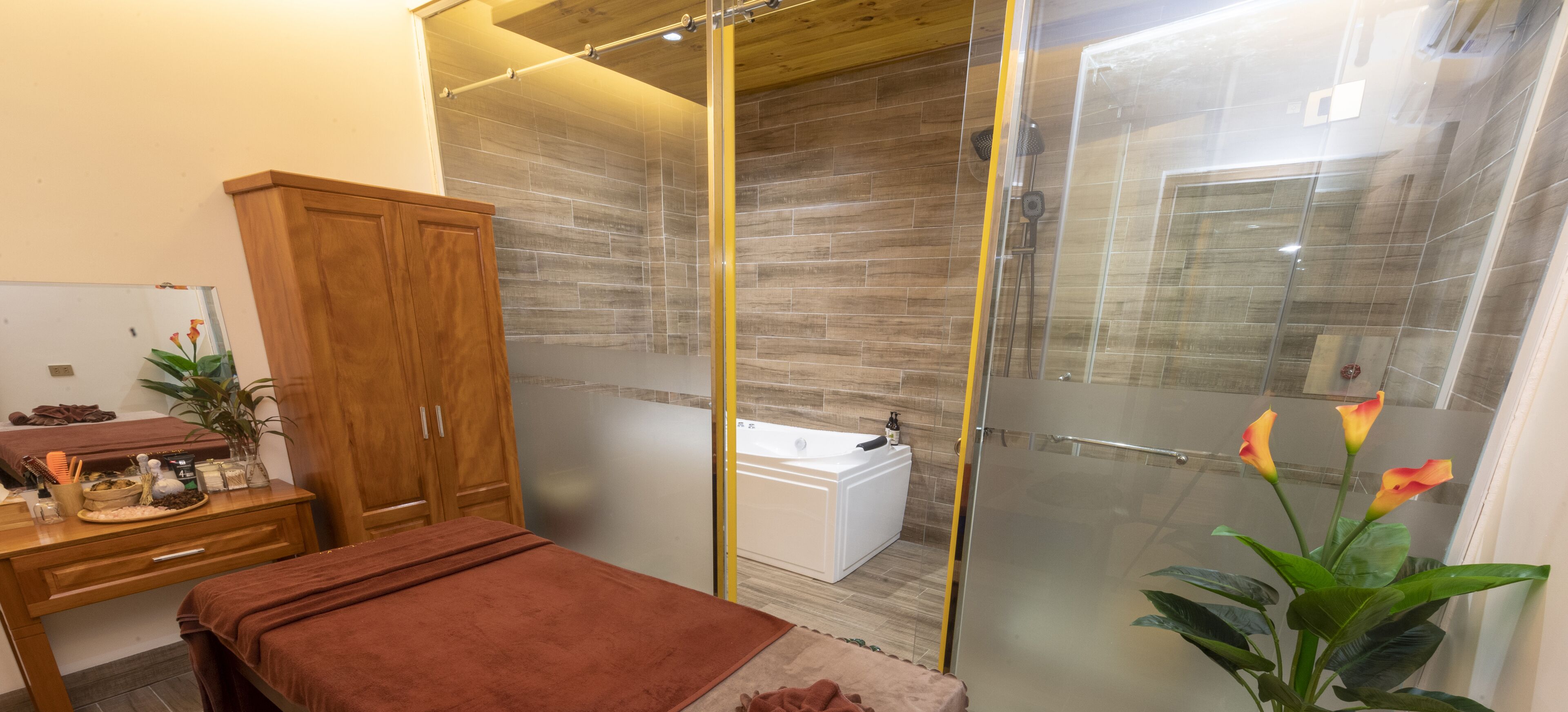 A modern bathroom with a glass shower enclosure, a wooden cabinet, a massage table, and a small white bathtub.