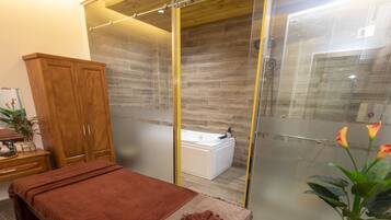 A modern bathroom with a glass shower enclosure, a wooden cabinet, a massage table, and a small white bathtub.