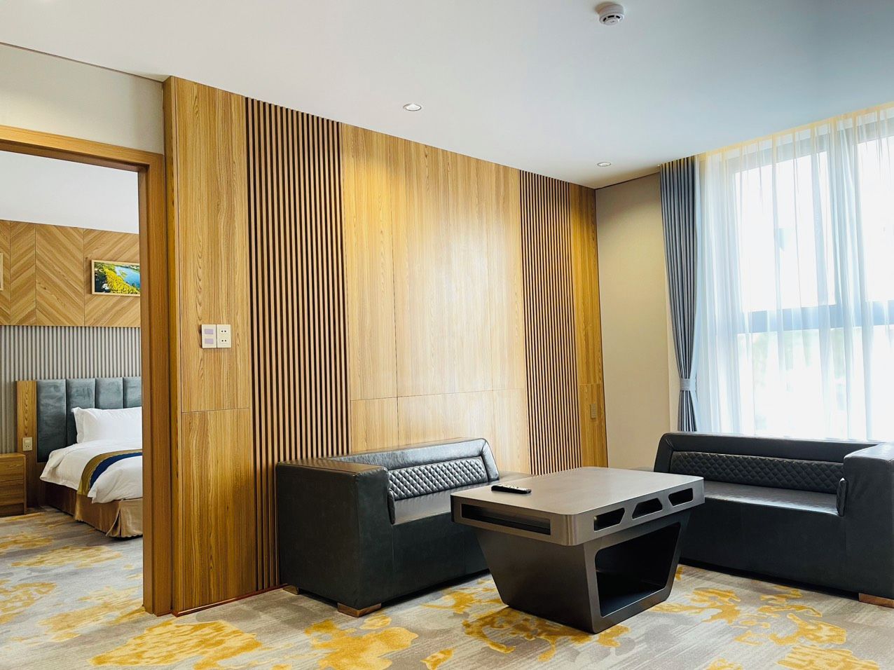 A modern hotel room with a bed, a sofa, a coffee table, and a large window with curtains.