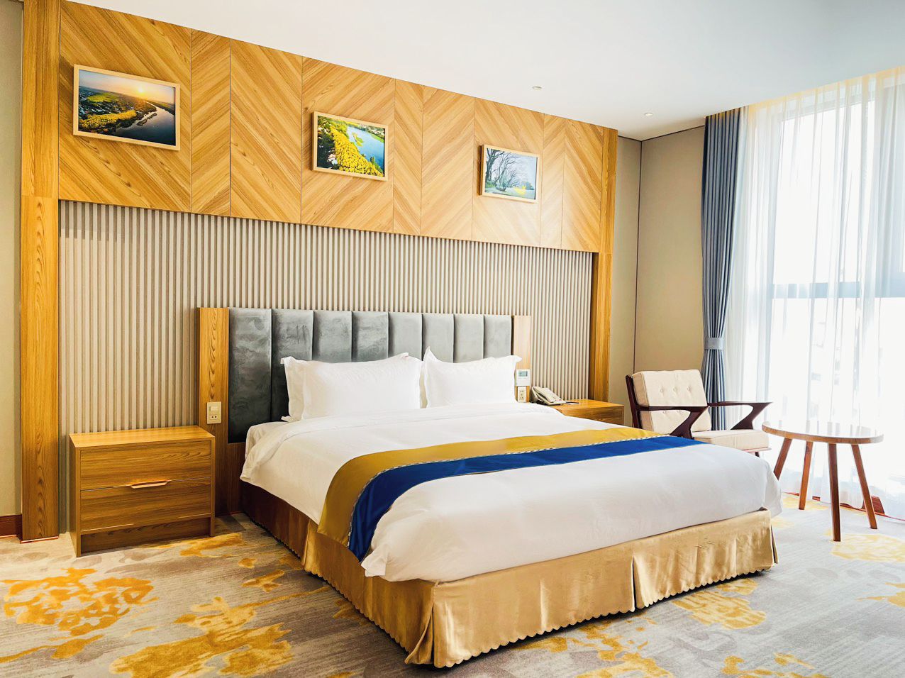 Hotellihuone, jossa on suuri sänky, yöpöytä, tuoli ja pieni pöytä.