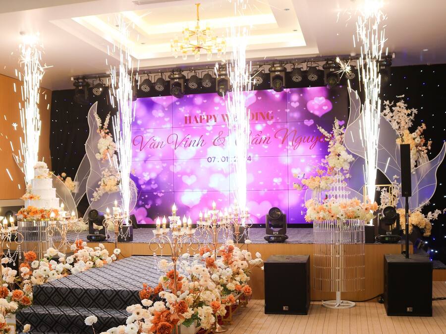 A stage with a 'Happy Wedding' backdrop, floral arrangements, and a chandelier.