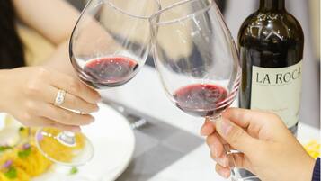 Dos personas sostienen copas de vino con una botella de vino La Rocca al fondo.