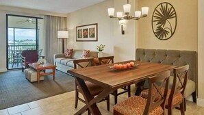 A hotel room with a dining table, sofa, and a balcony with a view.