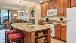 A kitchen with wooden cabinets, a granite countertop, a microwave, and a refrigerator.