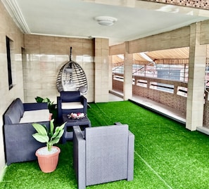 A covered outdoor seating area with a hanging chair, a sofa, and a table. - M & M Penthouse, 3 Bedrooms Salon Villa Complete
 (Abidjan)