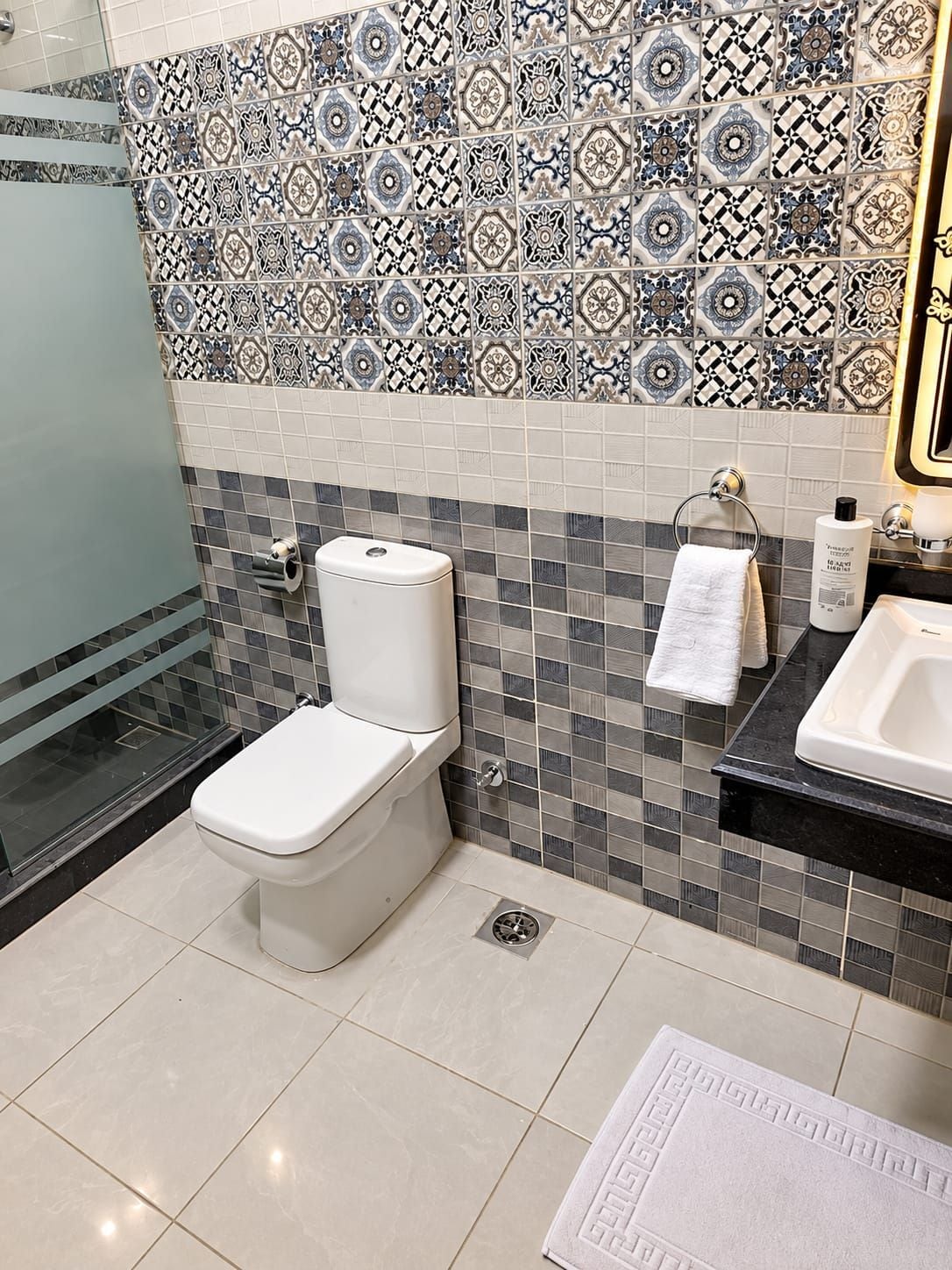 Un baño con inodoro, lavamanos y un salpicadero de azulejos estampados.