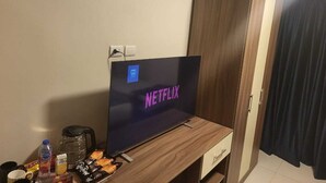 A room with a TV displaying the Netflix logo, a wooden cabinet, a small table with snacks, and a water bottle.