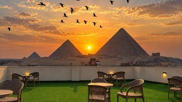 Una terraza en la azotea con césped artificial, mobiliario de mimbre y vistas a las pirámides al atardecer.