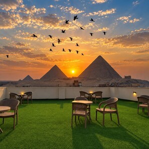 Una terraza en la azotea con césped artificial, mobiliario de mimbre y vistas a las pirámides al atardecer.