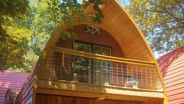 A wooden cabin with a balcony, a red door, and a small porch area. - Comfortable cabin in the mountains of North Carolina, located near TIEC. (Mill Spring)