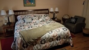 A bedroom with a bed, two bedside tables, a chair, a rug, and a wall painting. - Comfortable cabin in the mountains of North Carolina, located near TIEC. (Mill Spring)