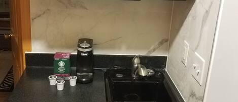 Uma cozinha compacta com micro-ondas de aço inoxidável, cafeteira e uma geladeira pequena.