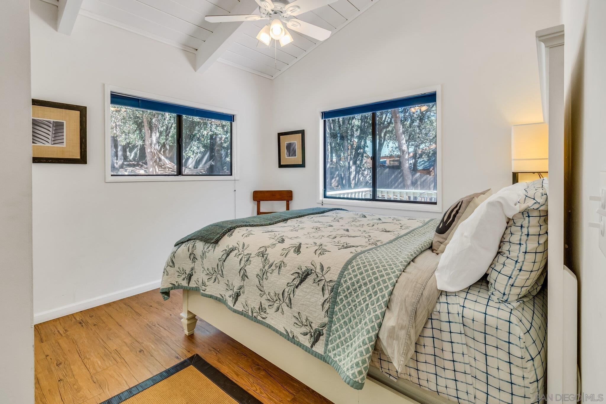 A bedroom with a bed, two windows, a ceiling fan, and a wooden floor.