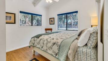 A bedroom with a bed, two windows, a ceiling fan, and a wooden floor.