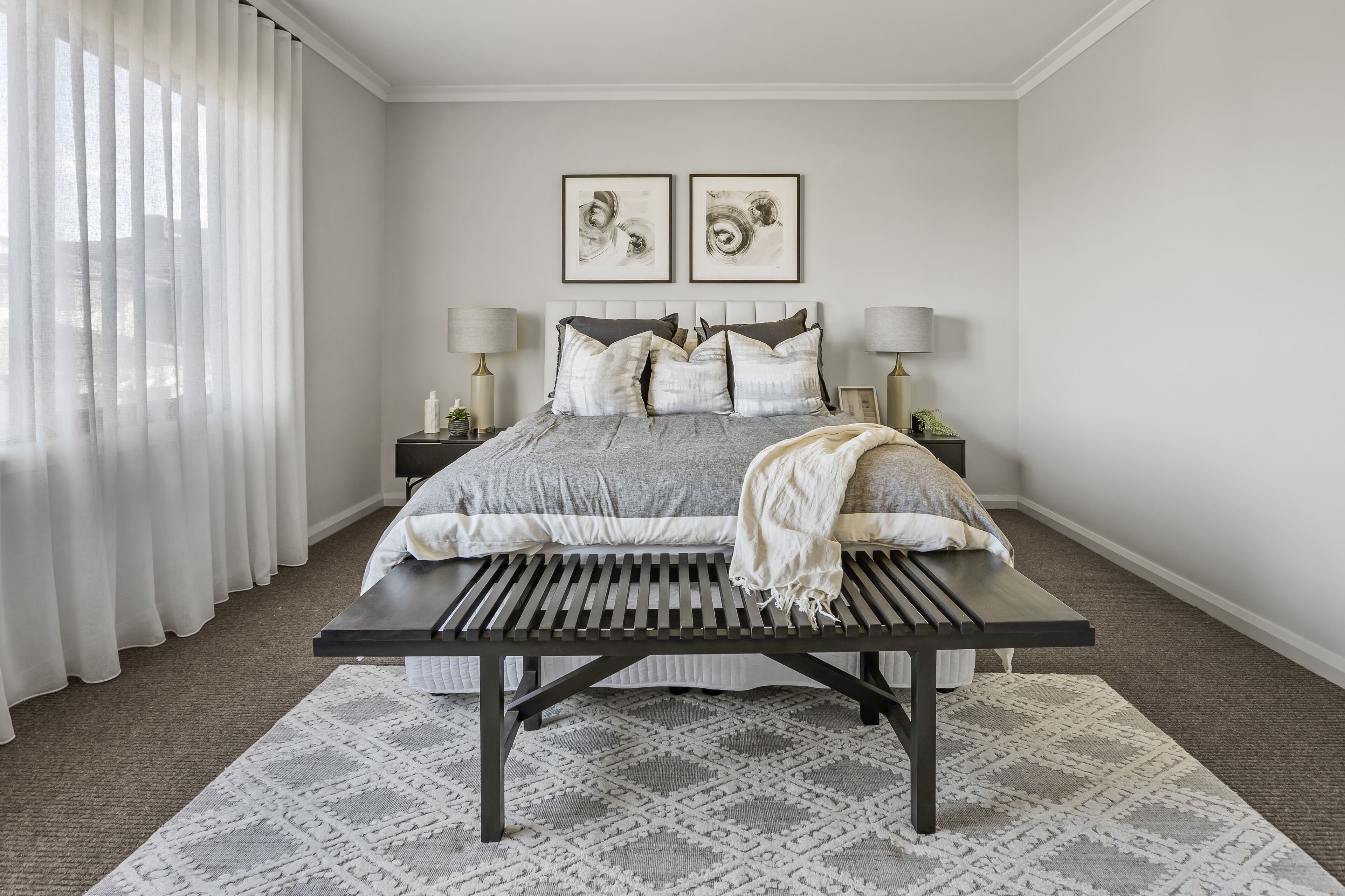 Een slaapkamer met een bed, twee nachtkastjes, een bankje en een kamerkleed met dessin.