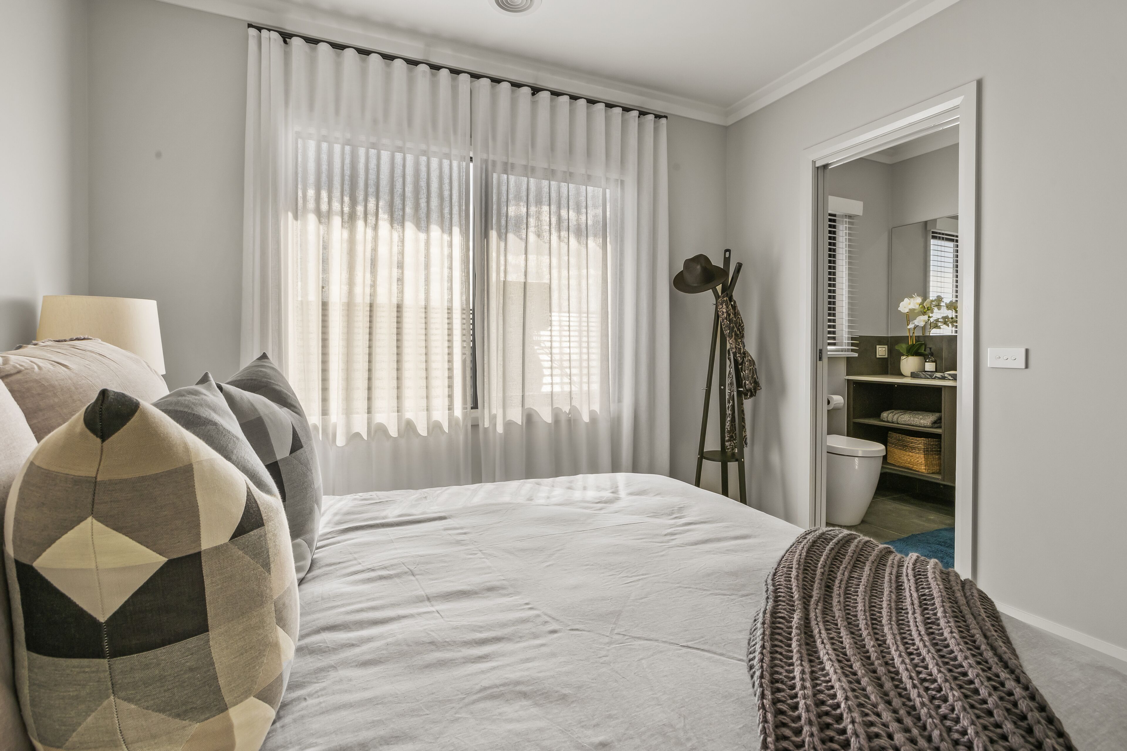 A bedroom with a bed, a bedside table, a lamp, a window with curtains, a wardrobe, and a mirror.