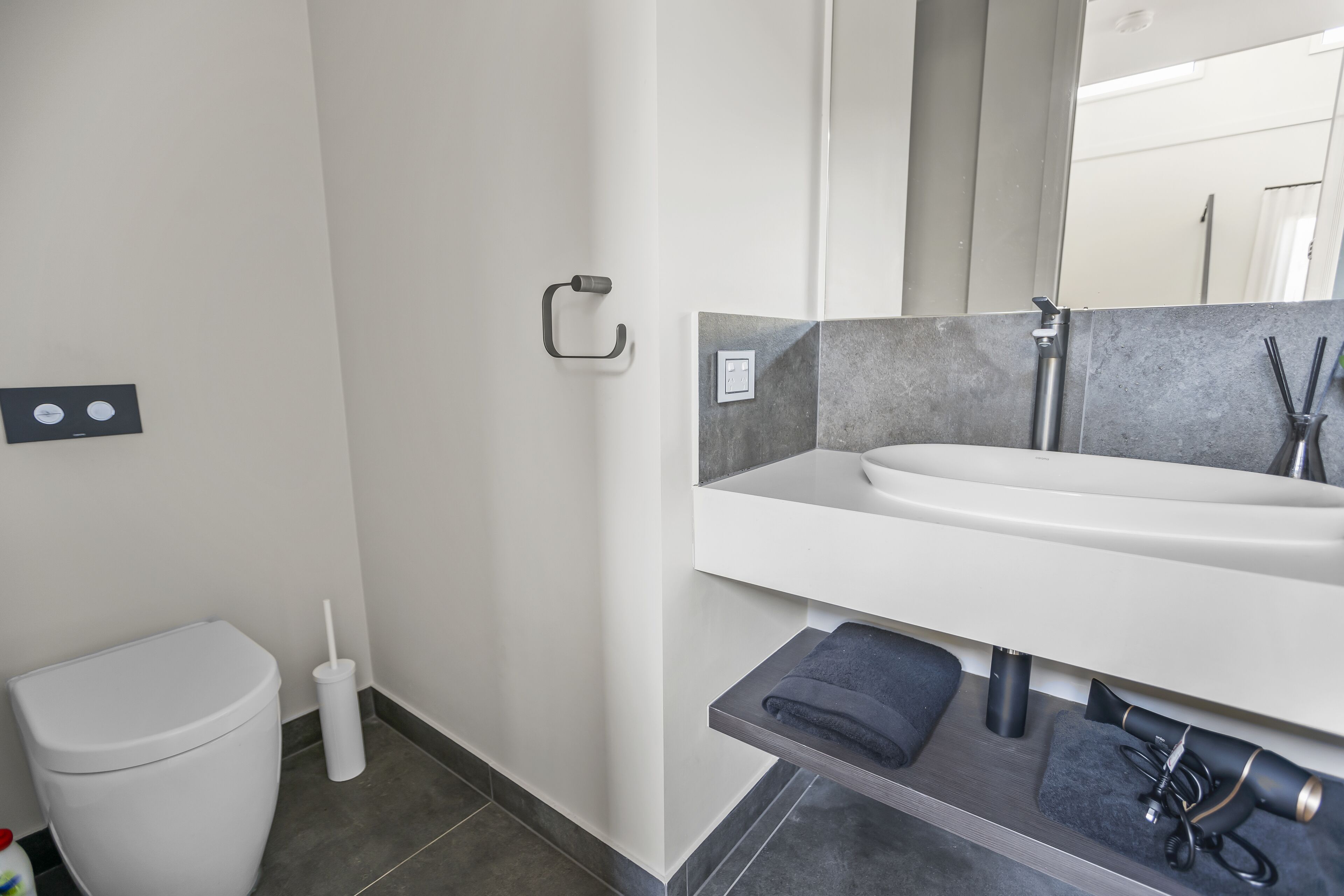 Un baño moderno con inodoro blanco, toallero, lavamanos y espejo.